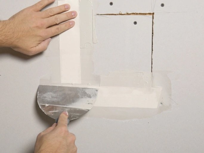 Handyman applying joint compound to a drywall repair in Delray Beach, FL